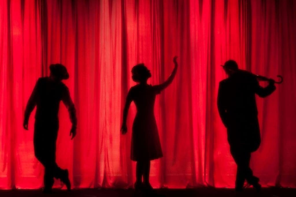 Three people standing behind a red curtain on a stage