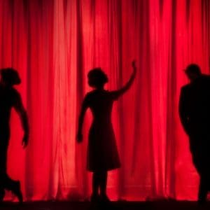 Three people standing behind a red curtain on a stage