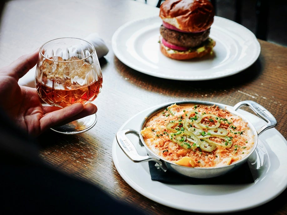 Two plates with food on them and a hand holding a glass