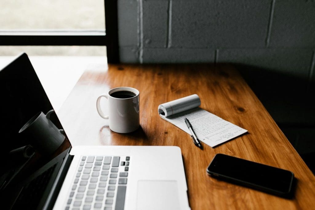 A laptop, mug, phone, and notepad on a desk.