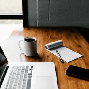 A laptop, mug, phone, and notepad on a desk.