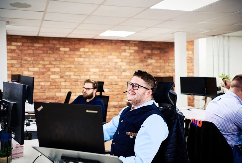 A person sat at a desk in front of a computer wearing a headset answering corporate accommodation queries.