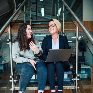 Team members sitting on stairs with laptop discussing work